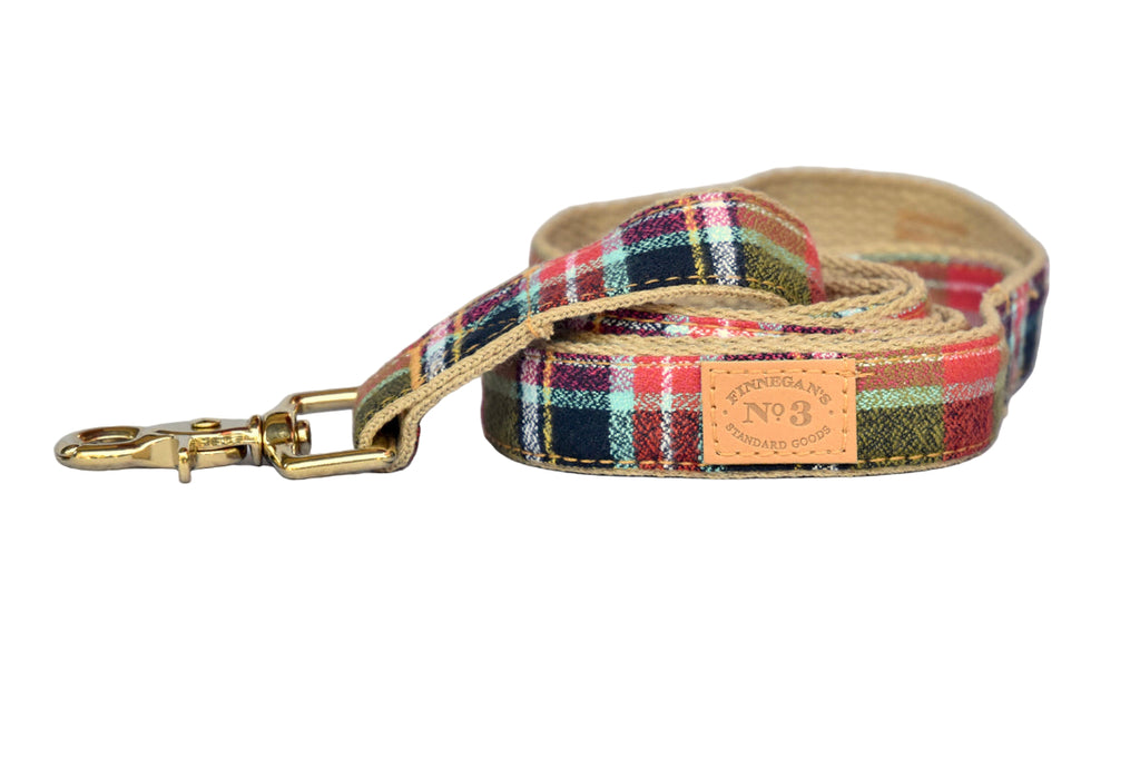 Plaid dog leash with brass clip on a wooden surface